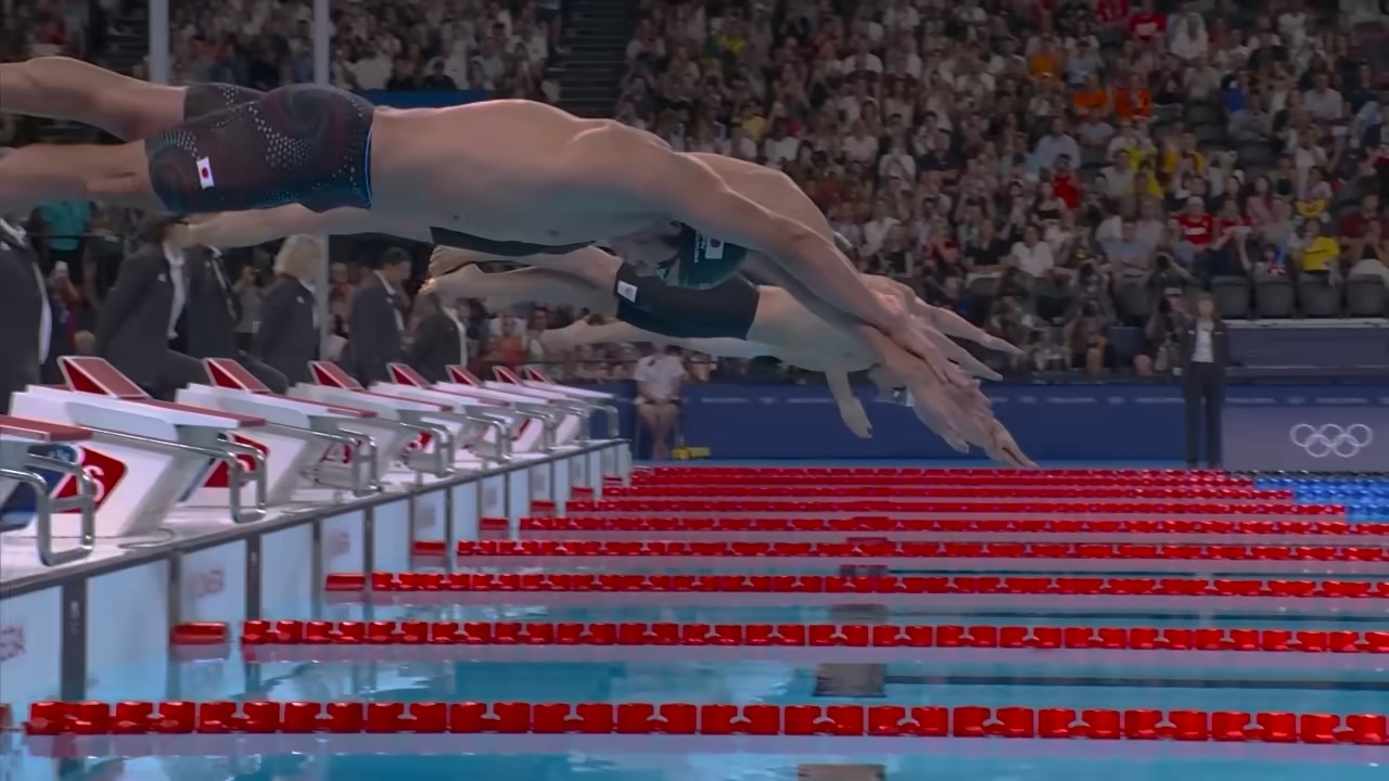 Competitive swimmers diving into an Olympic pool at the start of a race