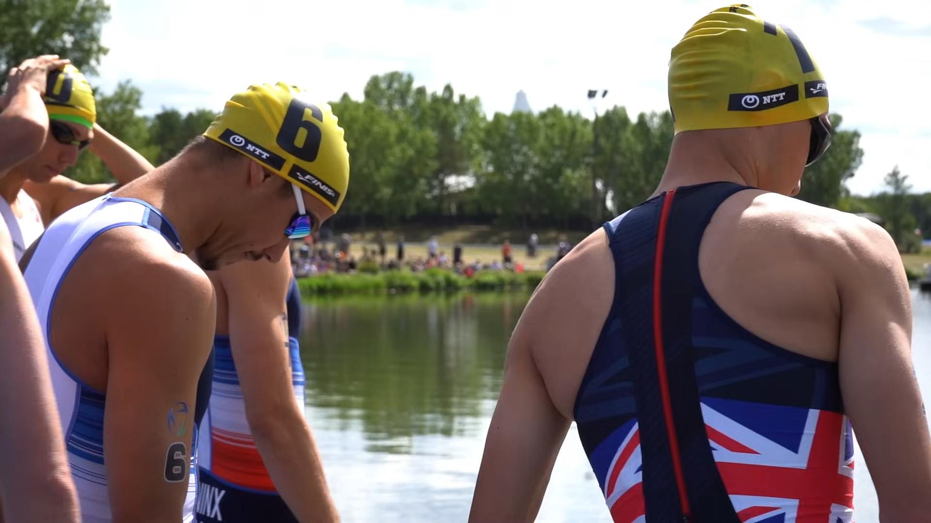 Triathletes in swim caps and race suits preparing by the water before a competition