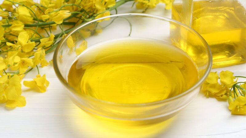 Canola oil sits in a glass bowl beside yellow canola flowers