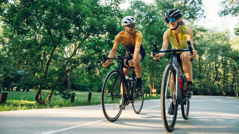 Two cyclists ride road bikes on a sunny tree-lined path