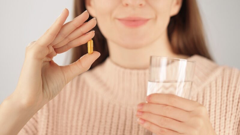 Person holds a supplement capsule and a glass of water before taking it