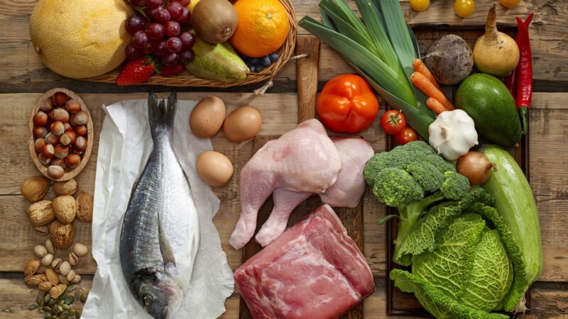 Paleo diet food list with fish, meat, eggs, fruit, nuts, and fresh vegetables on a wooden table