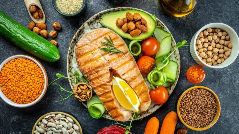 Grilled salmon with avocado, vegetables, nuts, seeds, and legumes on a dark table