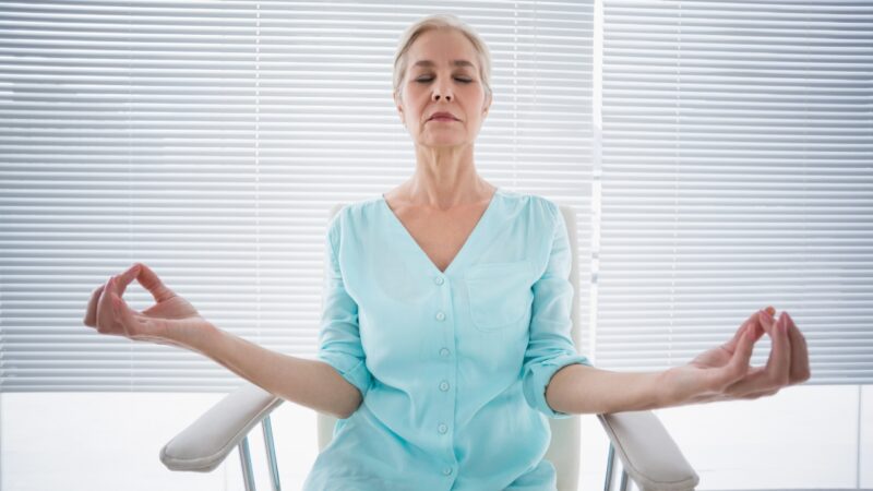 Senior woman practices chair yoga in a bright room