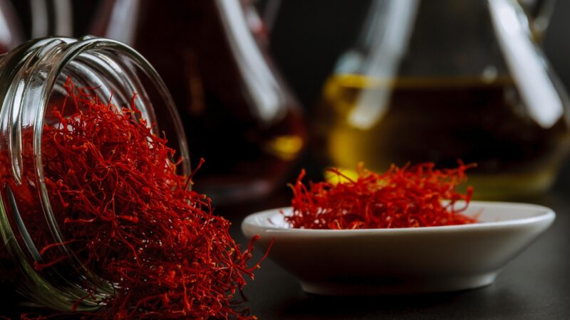 Safflower oil sits near bright red safflower threads in a small bowl