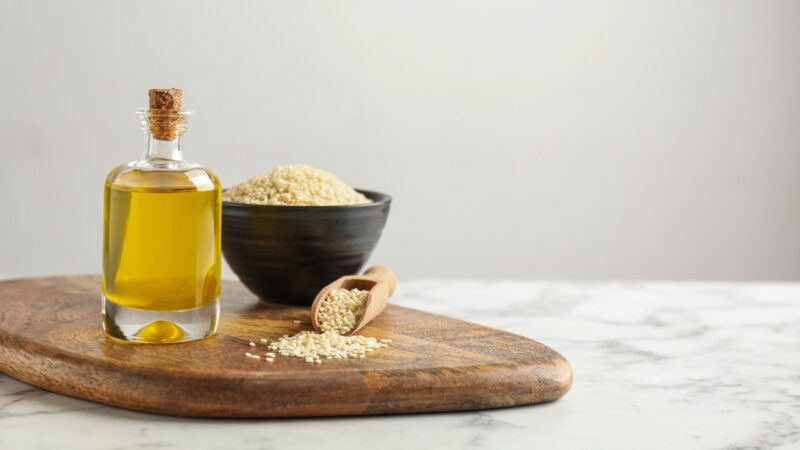 Sesame oil stands beside sesame seeds on a wooden board