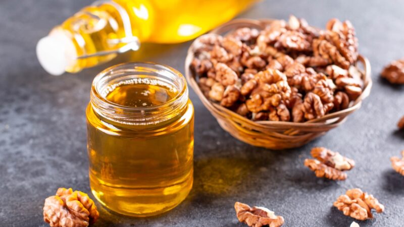 Walnut oil in a glass jar sits beside a bowl of walnuts