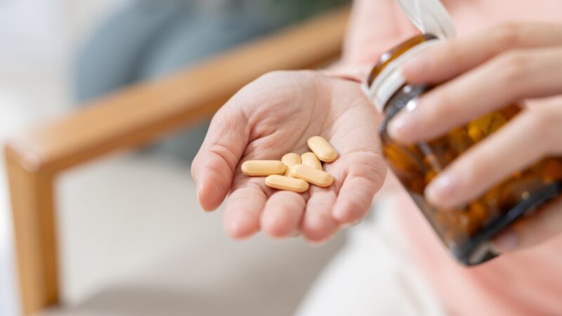 Person pours several tablets into their hand from a supplement bottle