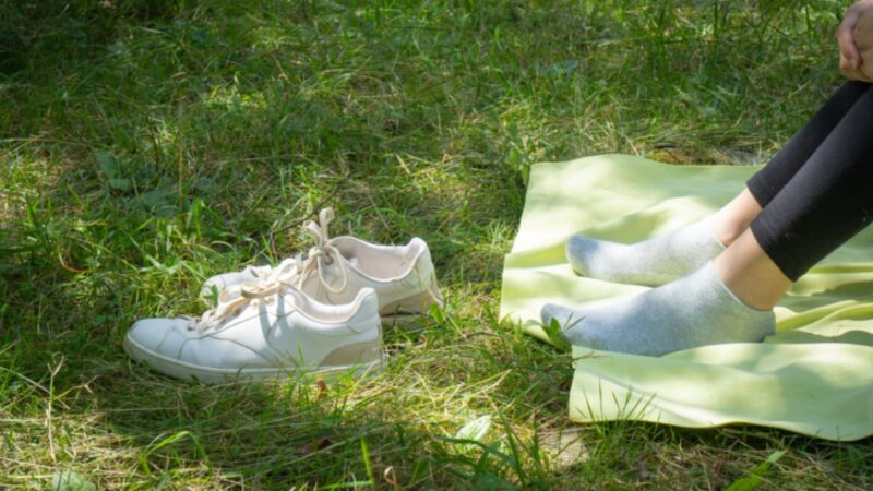 A person rests on a mat in the grass with white sneakers nearby