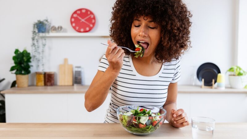 A woman eats a fresh salad at a kitchen table