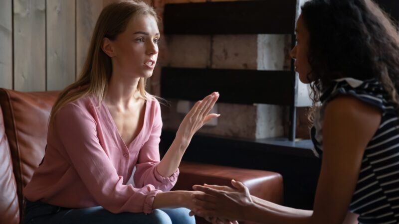Two women talk on a sofa about support and care