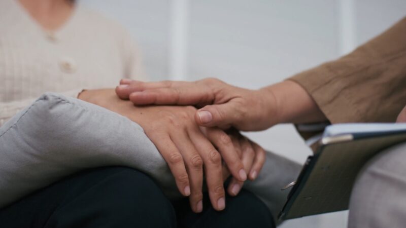 A counselor places a reassuring hand over another person’s hand during a support session