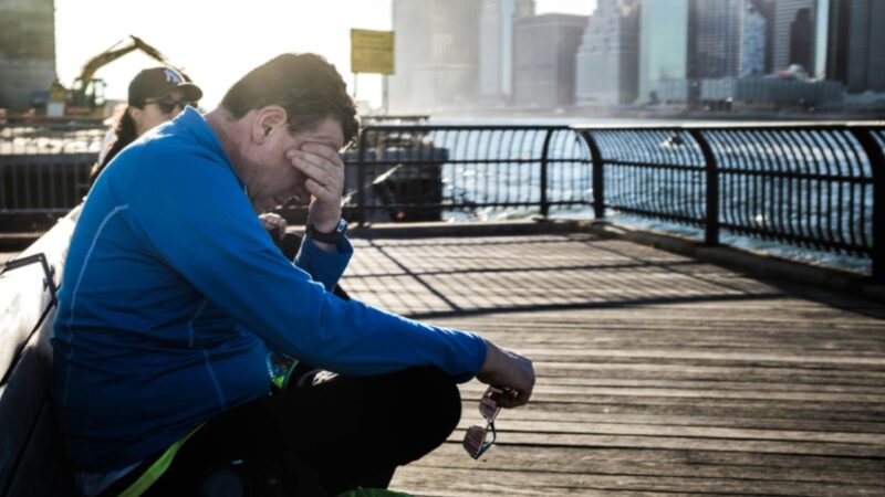 A man sits on a waterfront bench with his hand over his face