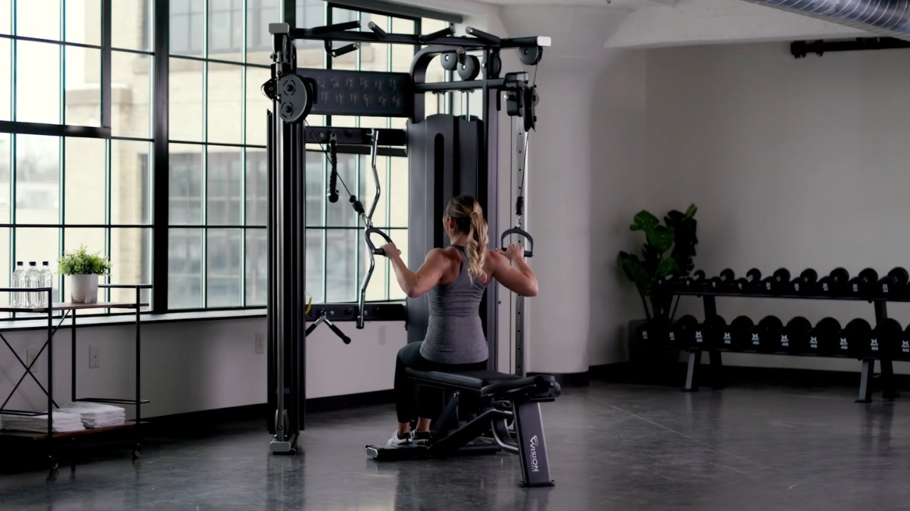 Woman uses a cable strength machine beside a rack of dumbbells