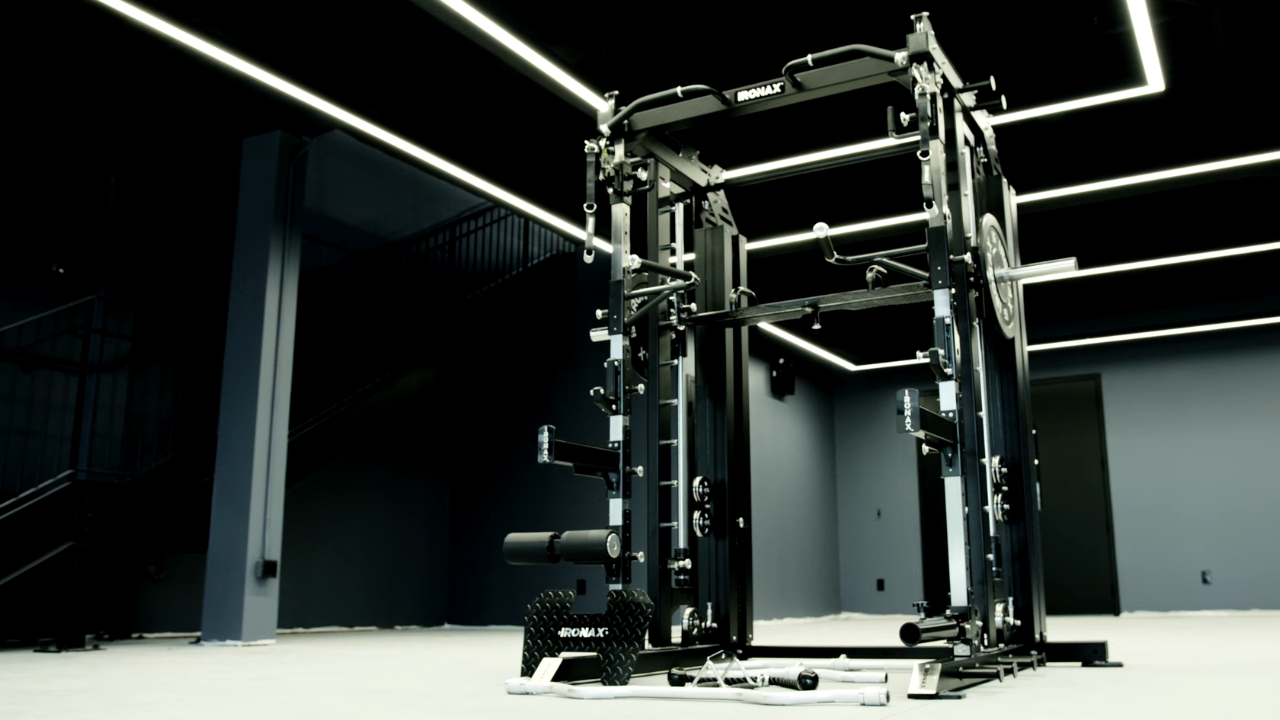 Ironax all-in-one strength machine with a bench and weight plates in a home gym