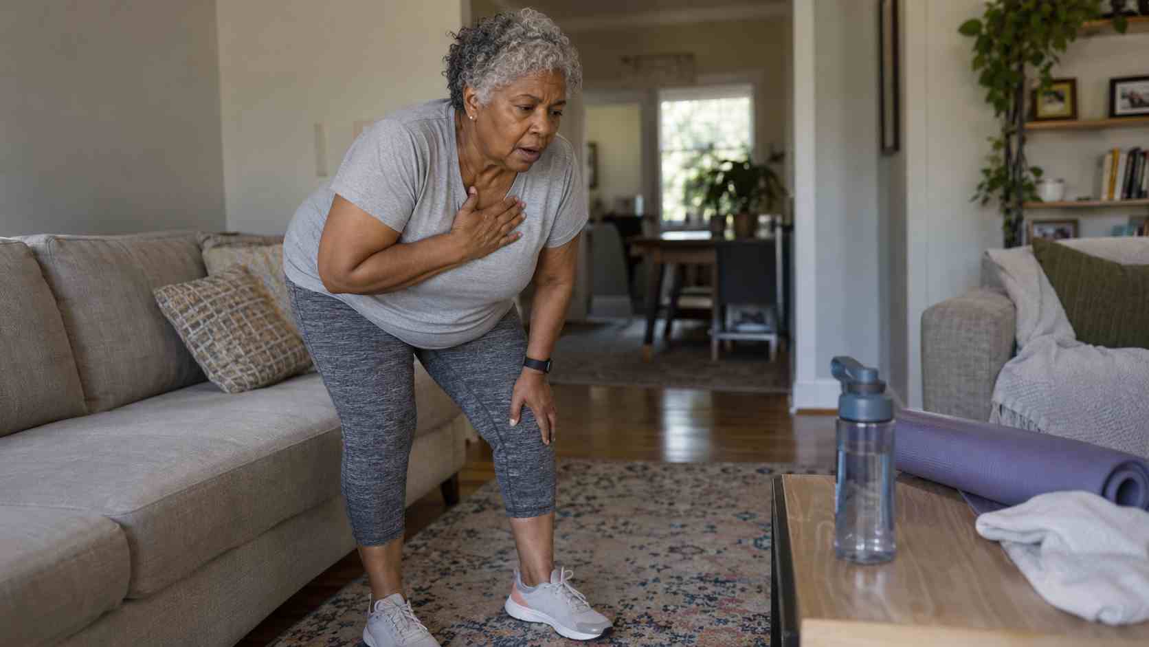 Older woman pausing during a home workout and catching her breath in the living room.